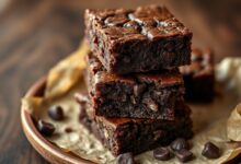 Quadrados de brownie com superfície craquelada brilhante, interior denso e úmido, servidos sobre prato rústico com lascas de chocolate