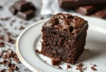 Vista de um bloco de brownie trufado cortado em fatias generosas, exibindo o interior ultra úmido e a superfície craquelada, com lascas de chocolate ao lado.
