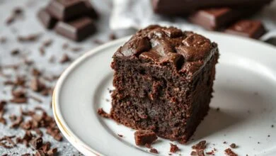 Vista de um bloco de brownie trufado cortado em fatias generosas, exibindo o interior ultra úmido e a superfície craquelada, com lascas de chocolate ao lado.