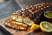 Filé de carne de jacaré dourado e suculento, com lascas de alho caramelizado e fatias de limão, servido em uma tábua de madeira rústica.