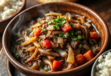 Carne seca desfiada e dourada, refogada com cebola grossa e tomate, finalizada com cheiro-verde fresco em um prato rústico.