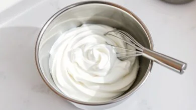 Tigela de aço inox com chantilly branco, firme e com picos suaves, demonstrando o resultado perfeito após a correção.