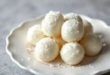 Quenelles de cocada branca mole de coco, úmidas e brilhantes, dispostas em um prato de porcelana branca.