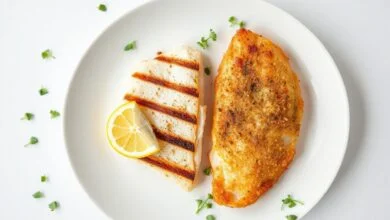 Dois filés de peixe lado a lado em um prato de fundo branco, mostrando a textura macia da merluza e a crocância da empanada da tilápia.