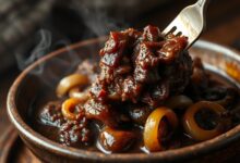 Costela de boi cozida na pressão, extremamente macia e desfiada, coberta por um molho escuro e encorpado com pedaços de cebola.