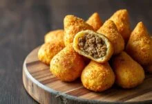 Coxinhas douradas e crocantes, com formato de gota, abertas para revelar o recheio de carne moída.