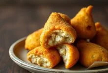 Coxinhas douradas com casca crocante, formato de gota perfeito, empilhadas em um prato rústico com recheio cremoso visível na mordida