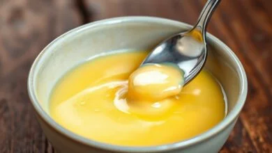 Creme inglês brilhante e denso, servido em tigela branca, com sementes de baunilha visíveis.