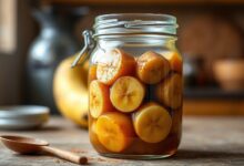 Um pote de vidro transparente repleto de doce de banana caseiro cremoso, com rodelas de banana caramelizadas visíveis e um brilho dourado acentuado pela manteiga e canela, pronto para ser servido.