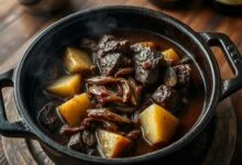 Um ensopado de carne com cerveja preta fumegante em uma panela de ferro fundo, com cubos de carne macia e desfiante, batatas em rodelas grossas, cebolas caramelizadas e folhas de louro, coberto por um molho escuro e encorpado.
