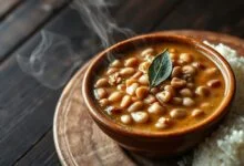 Tigela de feijão carioca cremoso, com caldo encorpado, grãos macios e folhas de louro, acompanhado de arroz branco fofinho.