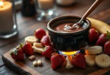 Panelinha de cerâmica com chocolate derretido brilhante e sedoso, rodeada de morangos vermelhos e rodelas de banana prontos para mergulhar.