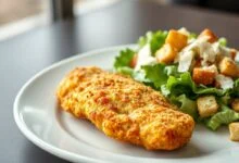 Prato finalizado com frango empanado dourado e crocante ao lado de uma salada Caesar verde e fresca, pronto para servir.