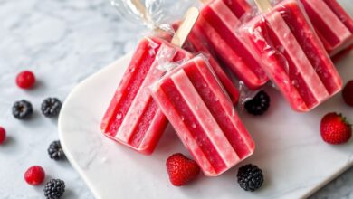 Arranjo vibrante de geladinhos de groselha vermelhos, alguns cortados para mostrar a textura cremosa, sobre superfície fria com gotas de água.
