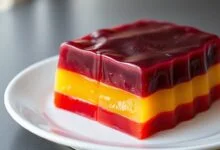A gelatina finalizada, desenformada em um prato, mostrando camadas perfeitas de morango, limão e uva.