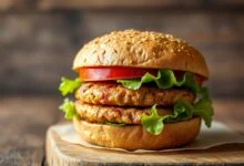 Hambúrguer de feijão com crosta dourada, firme, servido em pão com folhas verdes e tomate.