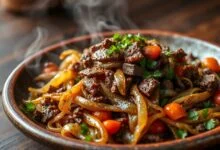 Carne-seca macia desfiada e refogada com cebola dourada, tomates e cheiro-verde, apresentada em um prato rústico.