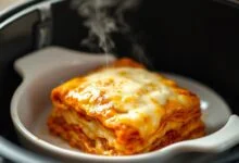 Lasanha gratinada com queijo dourado borbulhante, bordas crocantes e vapor subindo, servida em refratário de cerâmica dentro da cesta da airfryer