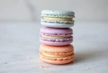 Torre de macarons em tons pastéis com cascas lisas, pés desenvolvidos e recheio visível.