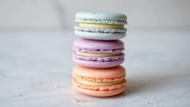 Torre de macarons em tons pastéis com cascas lisas, pés desenvolvidos e recheio visível.