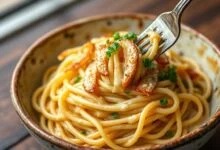 Espaguete al dente envolvido em emulsão cremosa de azeite, com fatias de alho dourado e salsinha fresca, servido em um prato rústico.