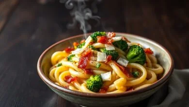 Prato principal de macarrão rigatoni com molho cremoso, raminhos de brócolis vibrantes e pedaços de bacon crocante.