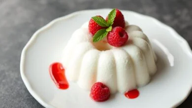 Manjar de coco fit perfeitamente desenformado, branco e aveludado, com textura firme e cremosa, decorado com frutas vermelhas.