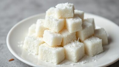 Cubos de maria-mole branca e fofa, cobertos com flocos de coco ralado, dispostos sobre um prato de porcelana.