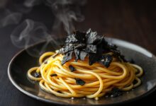 Espaguete al dente coberto com lâminas finíssimas de trufa negra e fio de azeite aromatizado, prato elegante sobre mesa de madeira escura.
