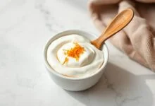 Tigela branca com molho cremoso de iogurte e laranja, com raspas de casca de laranja por cima e uma colher de madeira ao lado.