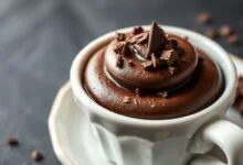 Mousse de chocolate escuro, aerado e brilhante, servido em travessa branca com raspas de chocolate e textura aveludada visível