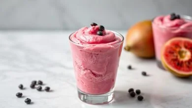 Mousse de goiaba de cor rosa vibrante, com textura aerada e cremosa, servida em um copo de vidro transparente, finalizada com sementes da fruta.