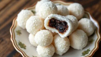 Uma tigela cheia de docinhos olho de sogra perfeitamente moldados, cobertos com açúcar cristal, com a ameixa escura visível no centro de um deles, convidando a comer.