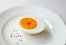 Um ovo perfeitamente cozido, cortado ao meio, revelando uma gema vibrante e cremosa, servido em um prato branco simples.