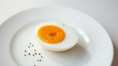 Um ovo perfeitamente cozido, cortado ao meio, revelando uma gema vibrante e cremosa, servido em um prato branco simples.