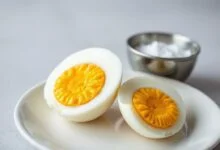 Um ovo cozido cortado ao meio, revelando uma gema amarela e cremosa no centro, com a clara branca e firme. O ovo está sobre um prato branco, pronto para ser comido.