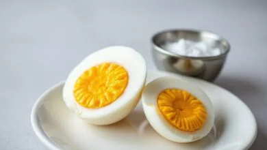 Um ovo cozido cortado ao meio, revelando uma gema amarela e cremosa no centro, com a clara branca e firme. O ovo está sobre um prato branco, pronto para ser comido.