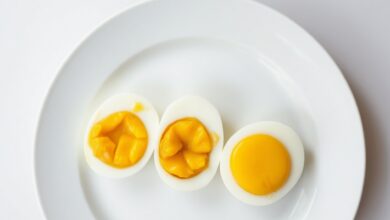 Três ovos cozidos cortados ao meio, revelando gemas com texturas diferentes — líquida, cremosa e firme — dispostos sobre um prato branco minimalista.