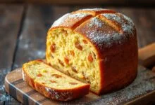 O panetone dourado, alto e perfeitamente assado, com a clássica fenda na parte superior, fatiado para revelar o miolo macio e repleto de frutas.