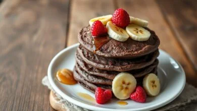Pilha de panquecas fit de cacau, fofinhas, com fatias de banana e frutas vermelhas ao lado.