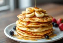 Pilha de panquecas douradas e finas, com textura de crepe, decoradas com fatias de banana caramelizada e um fio de mel.
