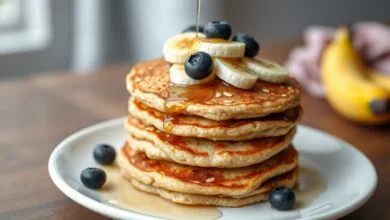 Pilha de panquequinhas douradas e fofas, cobertas com frutas frescas e mel.
