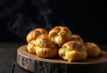 Uma fornada de pães de queijo dourados, com a casquinha rachada revelando o interior elástico e puxa-puxa.