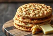 Pãezinhos integrais dourados e inflados, com casquinha crocante, empilhados sobre um prato de madeira rústico.