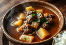 Tigela fumegante de picadinho com cubos de carne dourada, pedaços macios de mandioca e caldo encorpado, finalizado com salsinha fresca.
