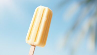 Um picolé de banana caseiro amarelo-claro, com textura cremosa e homogênea, perfeitamente desenformado em um palito branco, pronto para ser saboreado em um dia quente.