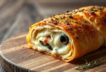 Uma pizza enrolada dourada, fatiada, com muçarela derretida escapando pelas bordas e orégano por cima, pronta para servir.