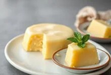 Pudim cremoso e dourado, fatiado em prato branco, com textura aveludada.