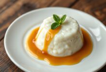 Pudim de tapioca dourado desenformado em prato branco, com calda de caramelo brilhante escorrendo pelas laterais, mostrando a textura cremosa do interior.