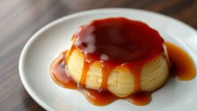 Um pudim de leite brilhante, com textura sedosa, desenformado em um prato branco e coberto por uma calda de caramelo líquida e escura.